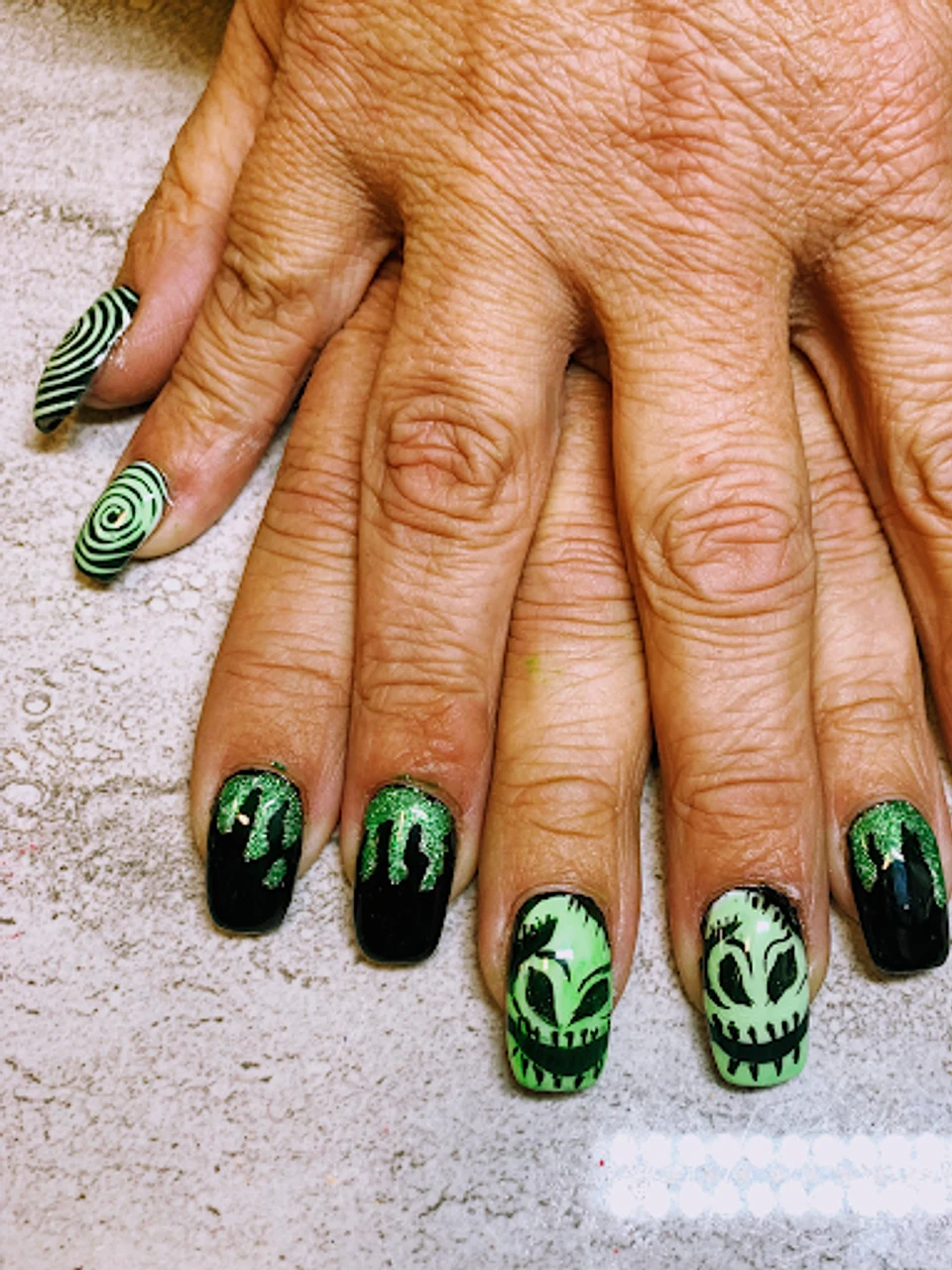 Halloween-themed green and black nail art with alien designs and glitter drip accents