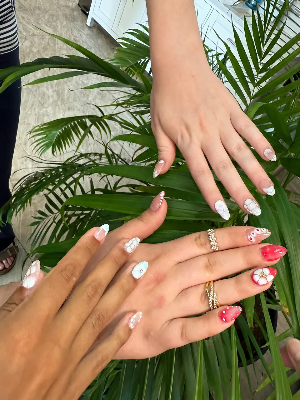 Three colorful nail-art sets posed together over palm leaves